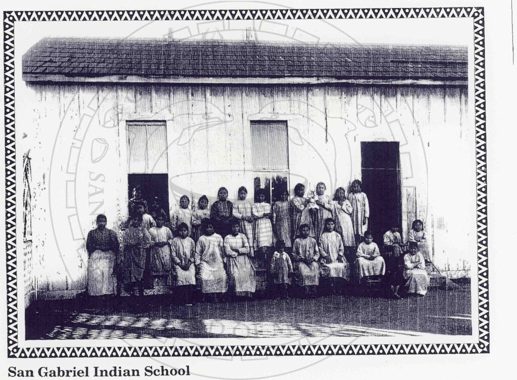 Black and white historical image of 26 young women and girls in dresses standing in front of a woman building
