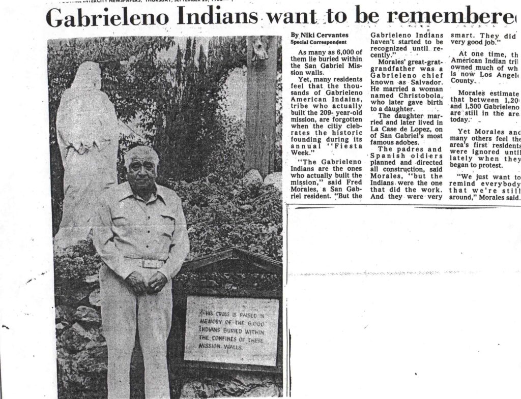 Facsimile of newspaper article entitled "Gabrieleno Indians Want to Be Remembered." Photo shows a man with white hair standing in front of a monument in a garden with a plaque reading: "This cross is raised in memory of the 6,000 Indians buried within the confines of these mission walls." Article quotes Fred Morales on his ancestry and the contributions of Native people to the mission.