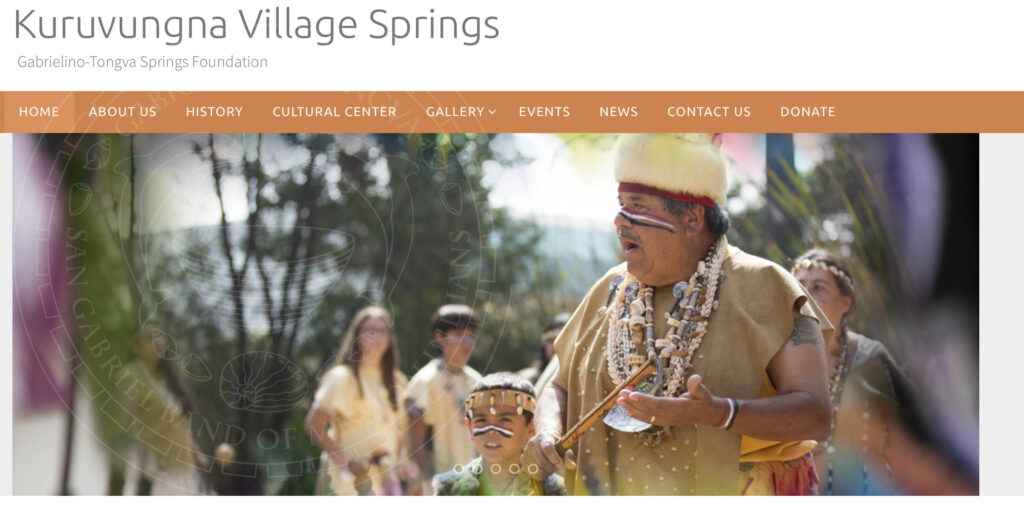 Man in traditional attire including fur headdress, necklaces and hide shirt uses a clapper stick while singing as youth in traditional attire follow him. Text at top reads "Kuruvungna Village Springs: Gabrielino-Tongva Springs Foundation" above buttons for web links Home, About Us, etc.