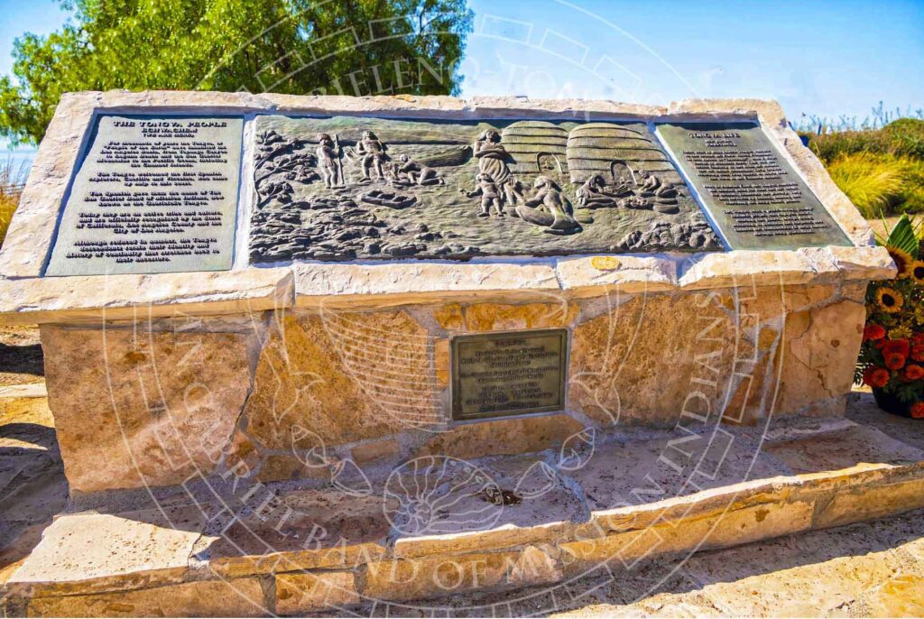 Stone monument with bronze frieze depicting historical Tribal members engaged in everyday activities in front of beehive-shaped houses. Title of text reads "The Tongva People."