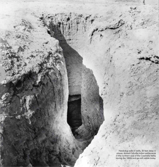 Black-and-white photograph of opening in ground with rough-hewn staircase winding down into a cavern