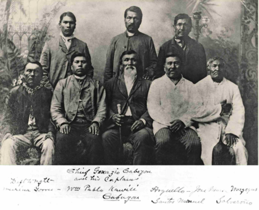Old photograph of eight men posed sitting and standing in formal 19th-century attire, centered around the white-bearded chief holding a walking stick