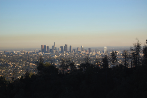 Silhouette of mountain and treeline with city skyline in background under a hazy sky
