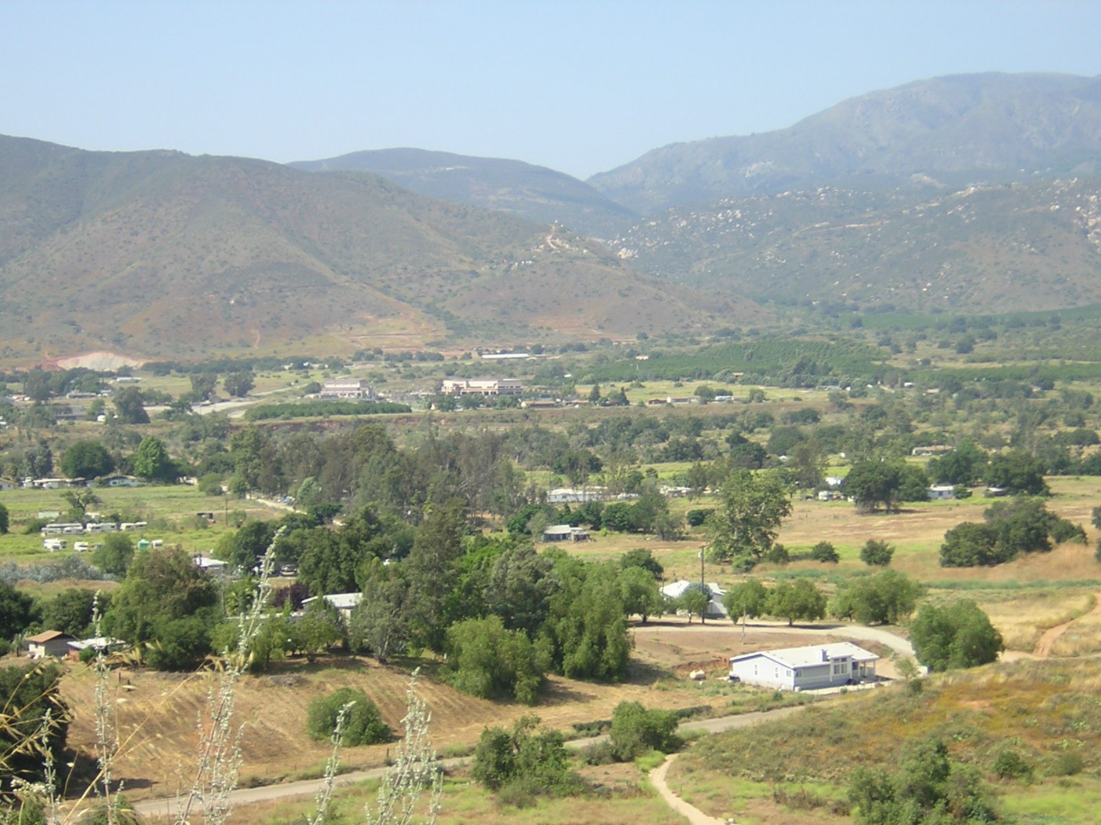 A lightly wooded valley surrounded by desert mountains with houses, roads, and agricultural fields