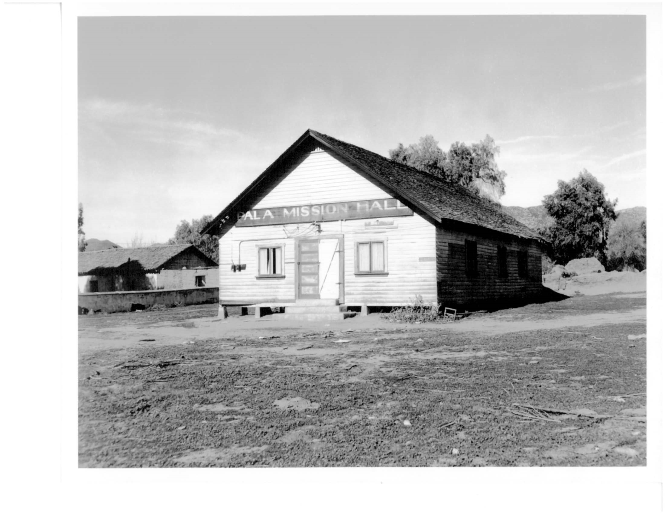 Old photograph of wooden building on piles with sign reading “Pala Mission Hall”