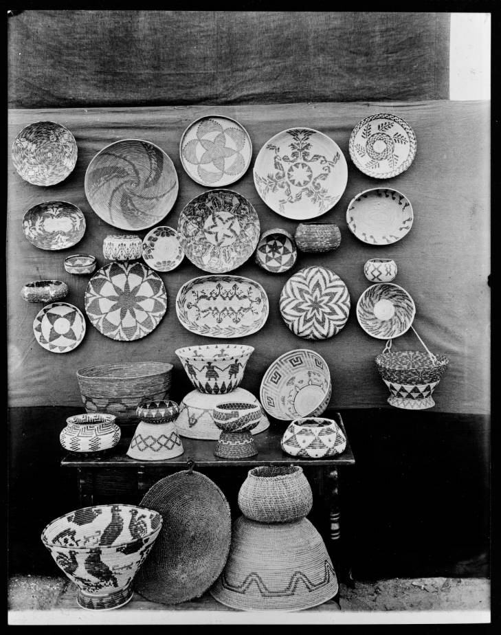 Black-and-white photograph of a collection on baskets with abstract and representational designs including stars, frets, spirals, birds, human figures and foliage patterns