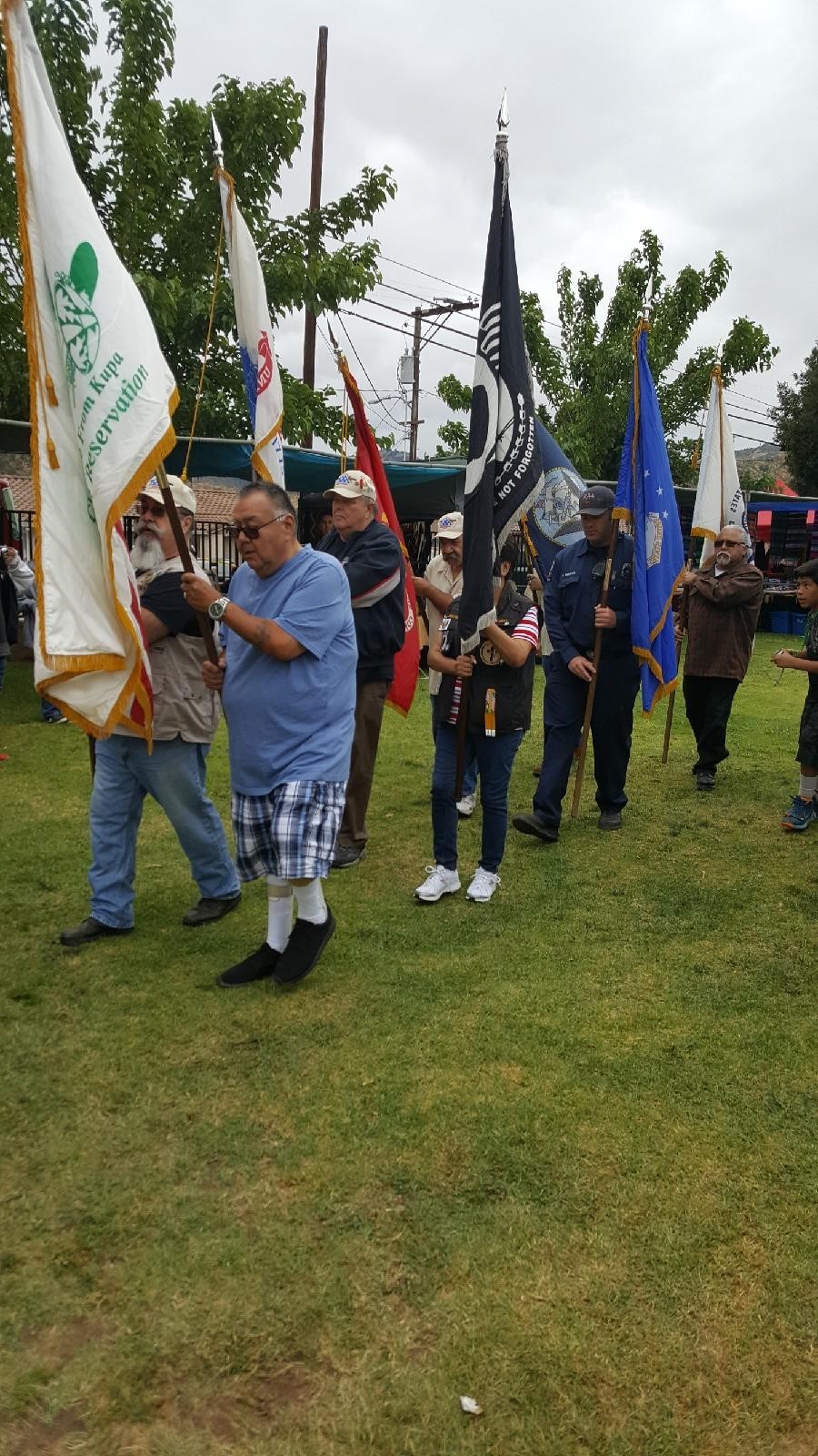 A procession of men in modern dress holding tribal and POW-MIA flags